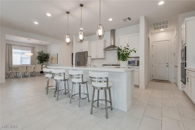 827 Klamath Springs St, Henderson, NV 89011 - kitchen with wall chimney range hood, a kitchen island with sink, appliances with stainless steel finishes, a breakfast bar area, and white cabinets