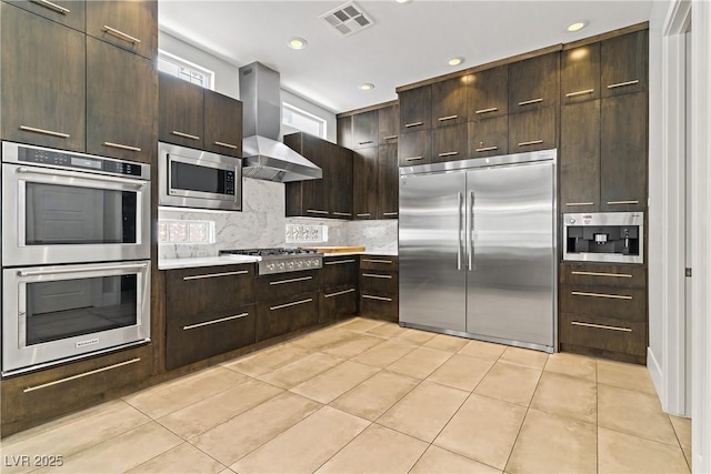 1509 Winslow St, Las Vegas, NV 89117 - kitchen featuring built in appliances, wall chimney exhaust hood, light tile patterned flooring, backsplash, and light countertops