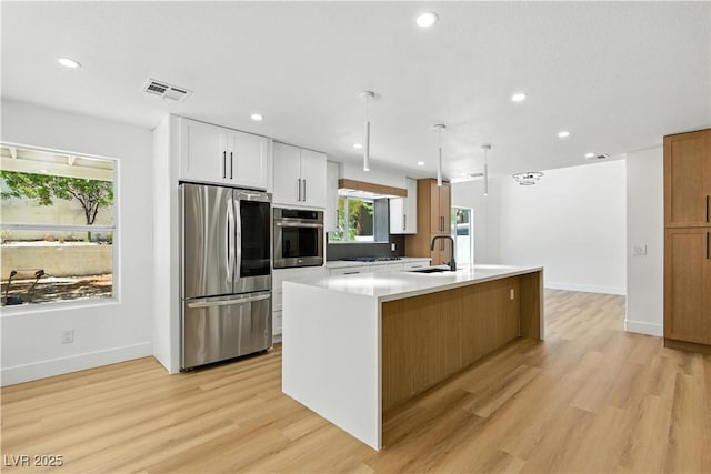 2105 Madagascar Ln, Las Vegas, NV 89117 - kitchen with appliances with stainless steel finishes, light wood-style flooring, white cabinets, light countertops, and a kitchen island with sink