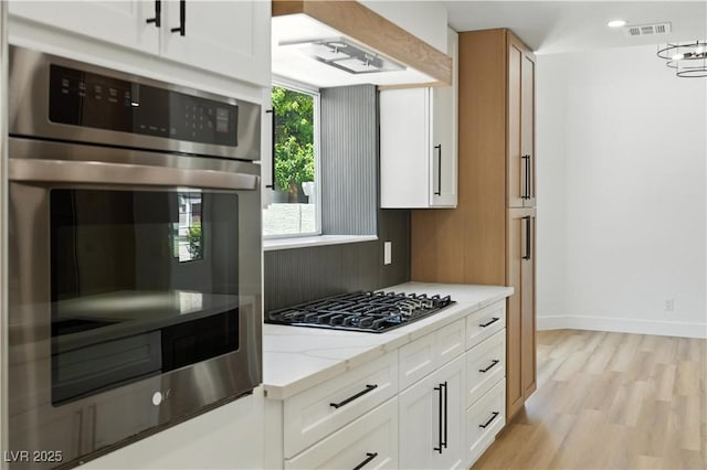 2105 Madagascar Ln, Las Vegas, NV 89117 - kitchen with black gas cooktop, light stone counters, white cabinets, light wood-type flooring, and stainless steel double oven