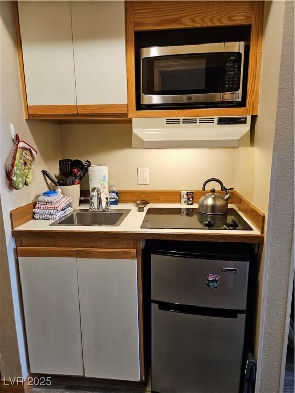 223 Hunter Ridge Rd Unit 121, Brian Head, UT 84719 - kitchen with stainless steel microwave, under cabinet range hood, black electric cooktop, white cabinets, and light countertops