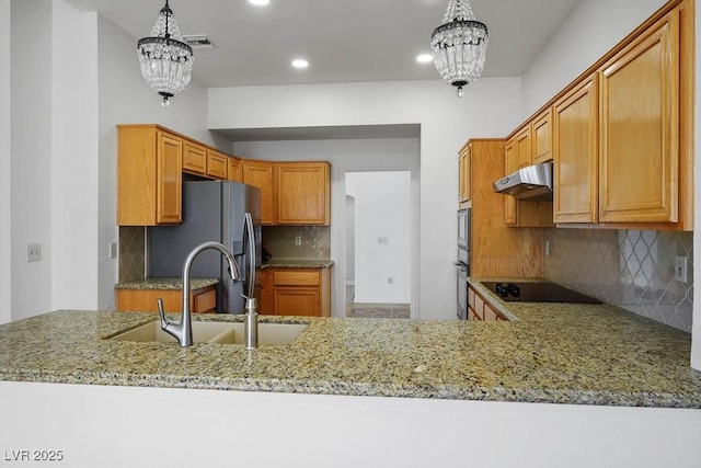 9704 Brawley Dr, Las Vegas, NV 89134 - kitchen featuring appliances with stainless steel finishes, under cabinet range hood, a chandelier, decorative backsplash, and light stone countertops