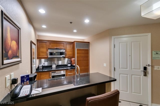 135 E Harmon Ave Unit 2821, Las Vegas, NV 89109 - kitchen featuring appliances with stainless steel finishes, brown cabinets, dark countertops, a peninsula, and a kitchen breakfast bar