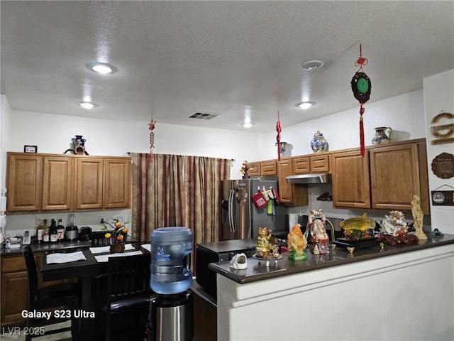 5651 Bettors Luck Ct, Las Vegas, NV 89122 - kitchen featuring stainless steel fridge with ice dispenser, dark countertops, under cabinet range hood, a textured ceiling, and brown cabinetry
