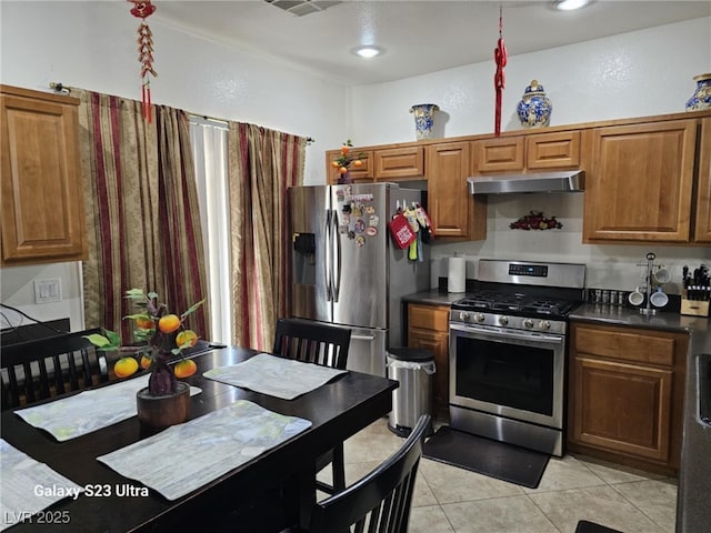 5651 Bettors Luck Ct, Las Vegas, NV 89122 - kitchen featuring appliances with stainless steel finishes, dark countertops, light tile patterned floors, under cabinet range hood, and brown cabinets