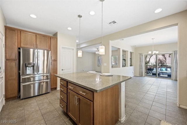 6713 Guidestar St, North Las Vegas, NV 89084 - kitchen featuring stainless steel fridge with ice dispenser, light tile patterned floors, light stone counters, a kitchen island, and brown cabinets