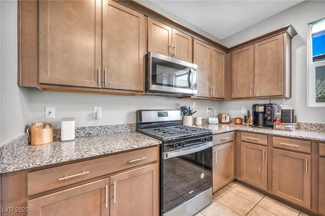 2024 Mystic Wave Rd, North Las Vegas, NV 89031 - kitchen featuring appliances with stainless steel finishes, light stone countertops, light tile patterned flooring, and brown cabinets