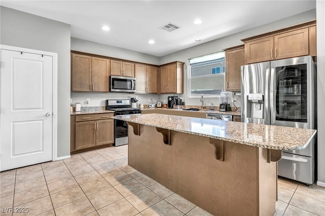 2024 Mystic Wave Rd, North Las Vegas, NV 89031 - kitchen featuring appliances with stainless steel finishes, light tile patterned floors, a kitchen bar, light stone counters, and a kitchen island