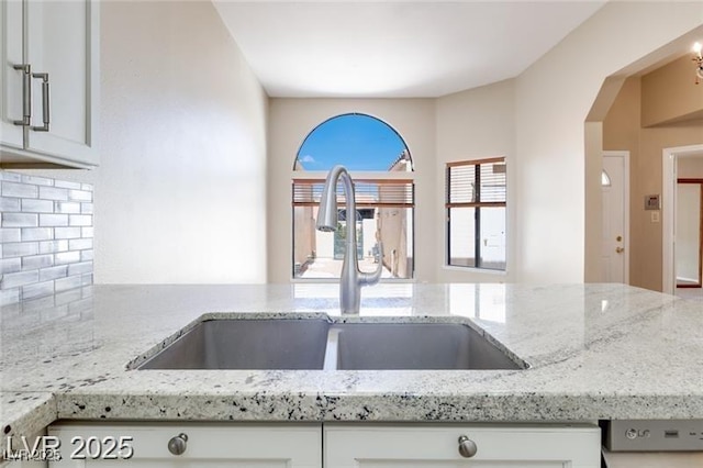 2723 Seabridge Dr, Las Vegas, NV 89121 - kitchen featuring backsplash, light stone countertops, white cabinetry, and arched walkways