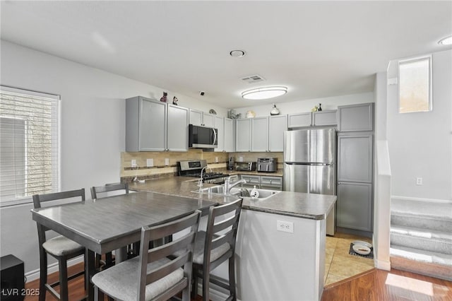 7640 Woven Memories St, Las Vegas, NV 89149 - kitchen with appliances with stainless steel finishes, a peninsula, tasteful backsplash, gray cabinets, and dark countertops