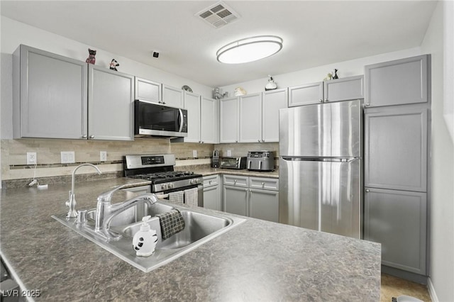 7640 Woven Memories St, Las Vegas, NV 89149 - kitchen featuring stainless steel appliances, tasteful backsplash, dark countertops, a peninsula, and gray cabinetry