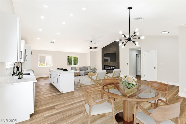 811 Spyglass Ln, Las Vegas, NV 89107 - dining room with a large fireplace, vaulted ceiling, a chandelier, light wood-type flooring, and a ceiling fan