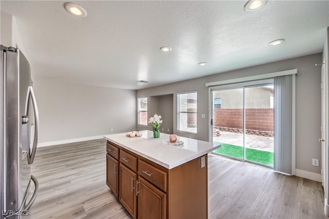 9129 Patrick Henry Ave, Las Vegas, NV 89149 - kitchen featuring stainless steel fridge, brown cabinets, light wood-type flooring, a kitchen island, and a textured ceiling