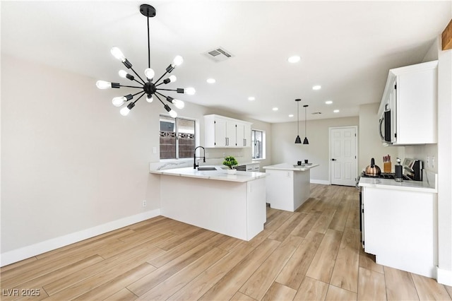 8113 Bay Springs Dr, Las Vegas, NV 89128 - kitchen featuring a peninsula, a kitchen island, light wood-type flooring, white cabinetry, and stainless steel microwave