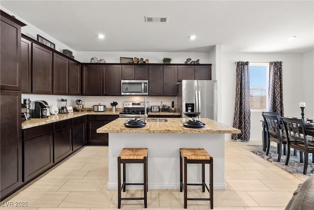 3568 E Malheur Ave, Pahrump, NV 89061 - kitchen featuring stainless steel appliances, dark brown cabinetry, a kitchen island with sink, light stone countertops, and recessed lighting