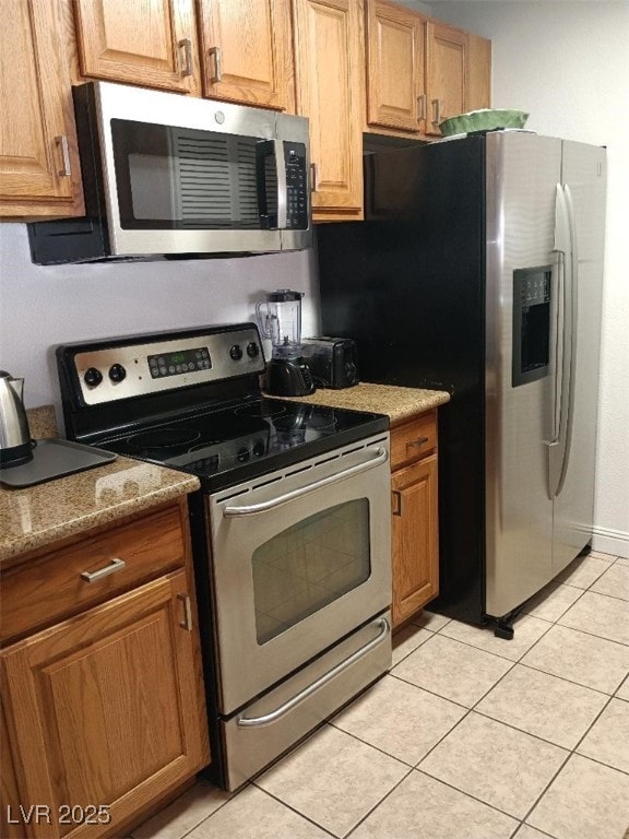 1515 E Reno Ave Unit D202, Las Vegas, NV 89119 - kitchen featuring stainless steel appliances, light tile patterned floors, stone counters, and brown cabinetry