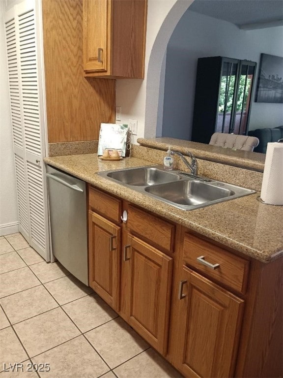 1515 E Reno Ave Unit D202, Las Vegas, NV 89119 - kitchen with stainless steel dishwasher, arched walkways, light tile patterned flooring, brown cabinets, and light countertops