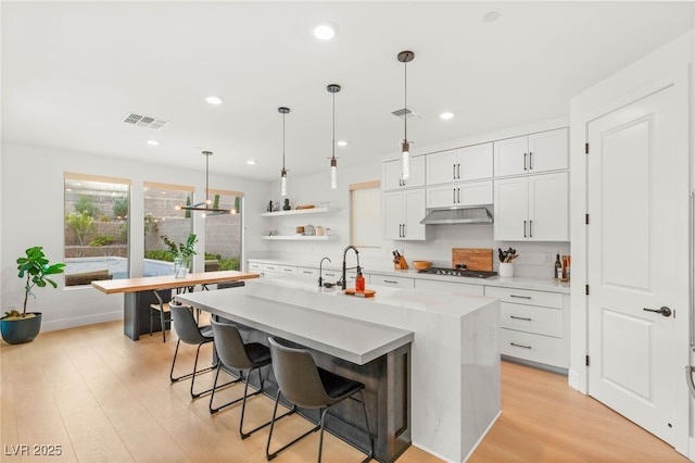 389 Red Feather Peak Ct, Las Vegas, NV 89138 - kitchen with open shelves, under cabinet range hood, an island with sink, light countertops, and white cabinets