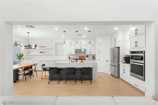 389 Red Feather Peak Ct, Las Vegas, NV 89138 - kitchen with stainless steel appliances, a breakfast bar, under cabinet range hood, open shelves, and light countertops