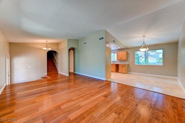 8729 Pesaro Dr, Las Vegas, NV 89117 - unfurnished living room with arched walkways, light wood-style floors, stairway, and a textured ceiling