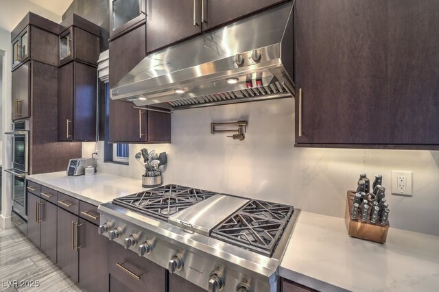 12544 Claymore Highland Ave, Las Vegas, NV 89138 - kitchen featuring ventilation hood, appliances with stainless steel finishes, light countertops, dark brown cabinetry, and glass insert cabinets