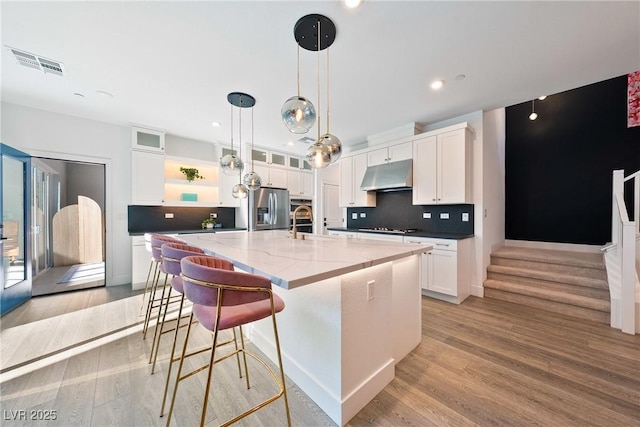 2722 Marchetti Pl, Henderson, NV 89044 - kitchen with stainless steel fridge with ice dispenser, under cabinet range hood, white cabinetry, backsplash, and light wood-style flooring