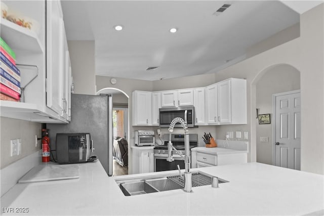 2512 Huber Heights Dr, Las Vegas, NV 89128 - kitchen with stainless steel appliances, arched walkways, white cabinets, light countertops, and recessed lighting