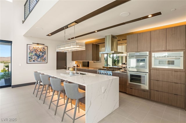 12 Desert Lake Ln, Henderson, NV 89011 - kitchen featuring island range hood, stainless steel appliances, modern cabinets, light stone counters, and a center island with sink