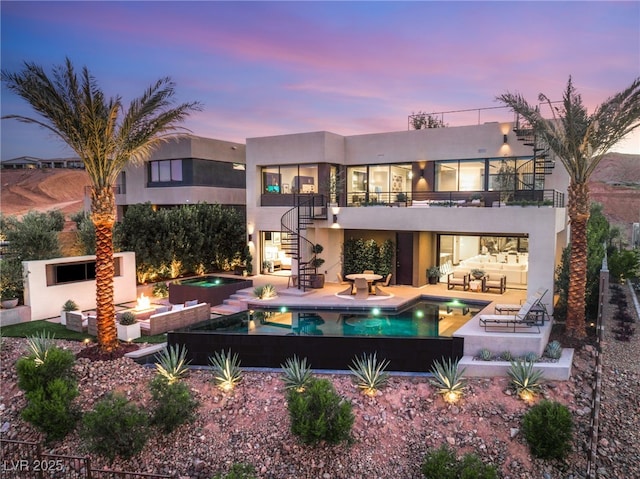 12 Desert Lake Ln, Henderson, NV 89011 - back of property at dusk featuring a balcony, an outdoor living space with a fire pit, stucco siding, stairs, and a patio area