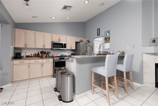 998 Hunters Run Dr, Henderson, NV 89002 - kitchen with appliances with stainless steel finishes, light brown cabinets, a breakfast bar, backsplash, and a peninsula
