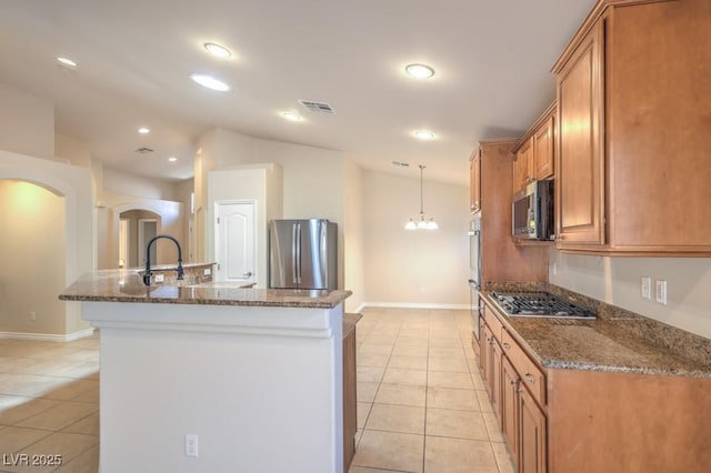 7998 Base Camp Ave, Las Vegas, NV 89178 - kitchen featuring appliances with stainless steel finishes, light tile patterned floors, brown cabinets, arched walkways, and a kitchen island with sink