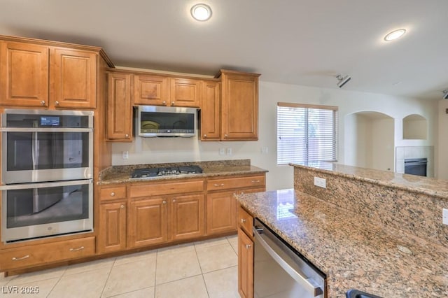 7998 Base Camp Ave, Las Vegas, NV 89178 - kitchen with appliances with stainless steel finishes, light stone countertops, brown cabinets, light tile patterned floors, and arched walkways