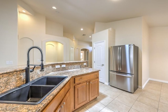7998 Base Camp Ave, Las Vegas, NV 89178 - kitchen with freestanding refrigerator, light tile patterned floors, arched walkways, recessed lighting, and brown cabinetry