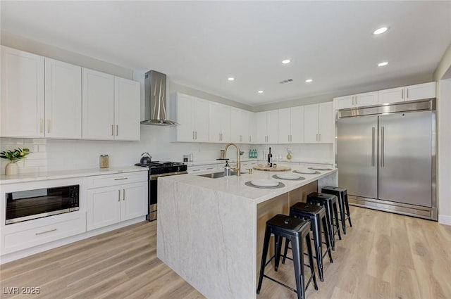 9632 Cherry Canyon Ave, Las Vegas, NV 89129 - kitchen with wall chimney range hood, stainless steel appliances, a breakfast bar, light wood-style floors, and white cabinetry