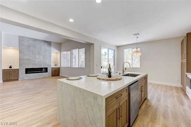 9632 Cherry Canyon Ave, Las Vegas, NV 89129 - kitchen featuring stainless steel dishwasher, light wood-style floors, a large fireplace, an island with sink, and light stone counters