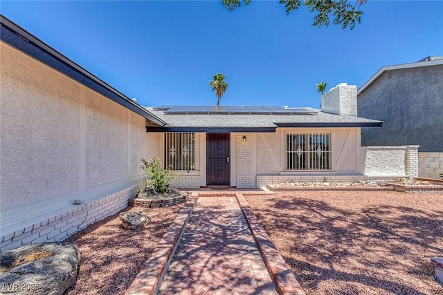 6808 Waterhen Cir, Las Vegas, NV 89108 - view of exterior entry with roof mounted solar panels, brick siding, a chimney, and stucco siding