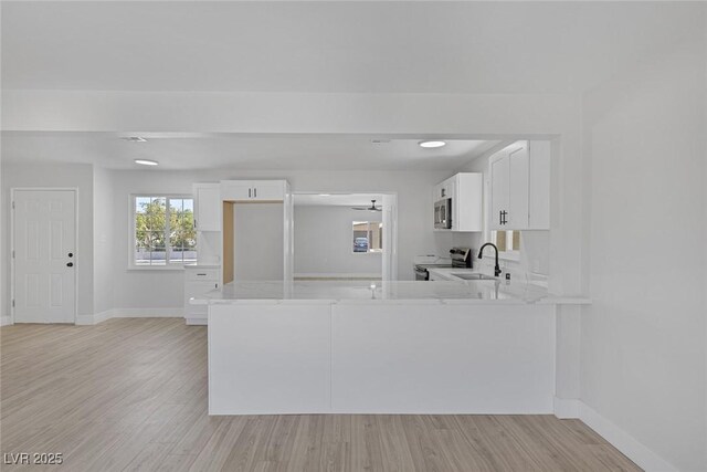 2005 Jansen Ave, Las Vegas, NV 89101 - kitchen with appliances with stainless steel finishes, white cabinets, a peninsula, light wood-style floors, and light stone counters