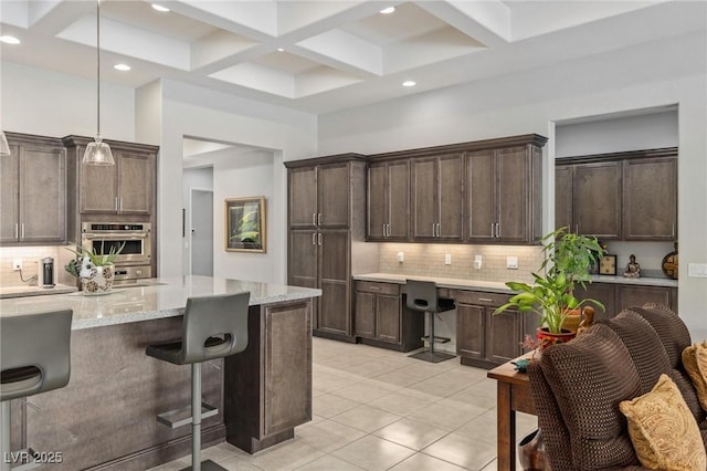 6315 Carol Butte Ct, Las Vegas, NV 89141 - kitchen featuring coffered ceiling, backsplash, dark brown cabinets, a kitchen breakfast bar, and light tile patterned floors