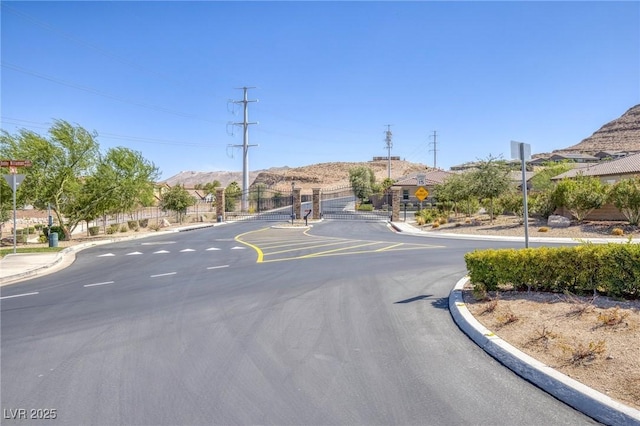 6315 Carol Butte Ct, Las Vegas, NV 89141 - view of asphalt road featuring traffic signs, curbs, a gate, a mountain view, and a gated entry