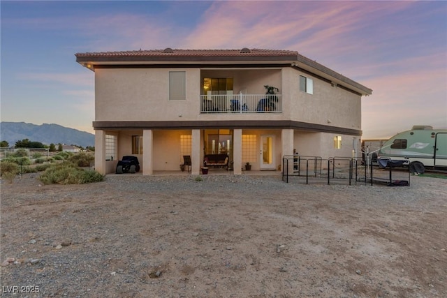 3821 Tumbleweed Ave, Pahrump, NV 89048 - back of property at dusk with a balcony, stucco siding, a patio area, and a mountain view