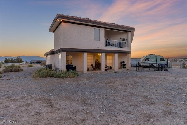 3821 Tumbleweed Ave, Pahrump, NV 89048 - back of property at dusk with a balcony, stucco siding, a patio area, a mountain view, and a tiled roof