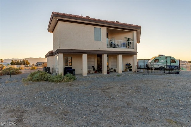 3821 Tumbleweed Ave, Pahrump, NV 89048 - back of house at dusk featuring a balcony, stucco siding, a tile roof, and a patio area