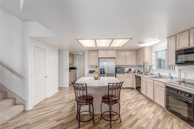 3821 Tumbleweed Ave, Pahrump, NV 89048 - kitchen with black appliances, light wood-style floors, a kitchen island, and a breakfast bar