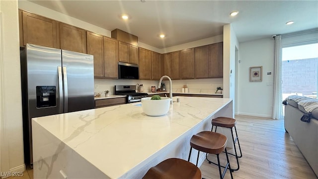 739 Wild Highlands Ln, Henderson, NV 89015 - kitchen with appliances with stainless steel finishes, light wood-type flooring, light stone countertops, a kitchen island with sink, and a breakfast bar