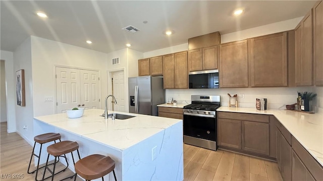 739 Wild Highlands Ln, Henderson, NV 89015 - kitchen featuring stainless steel appliances, light wood-style floors, a kitchen breakfast bar, a center island with sink, and light stone counters