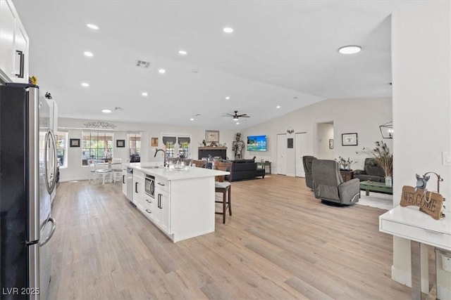 7675 Butterscotch Ct, Las Vegas, NV 89131 - kitchen with appliances with stainless steel finishes, a breakfast bar, vaulted ceiling, white cabinetry, and light wood-style flooring