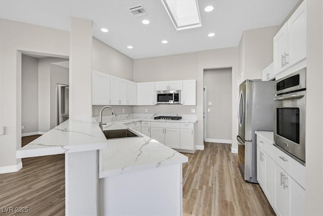 10700 Button Willow Dr, Las Vegas, NV 89134 - kitchen with appliances with stainless steel finishes, a peninsula, light wood finished floors, white cabinets, and light stone countertops