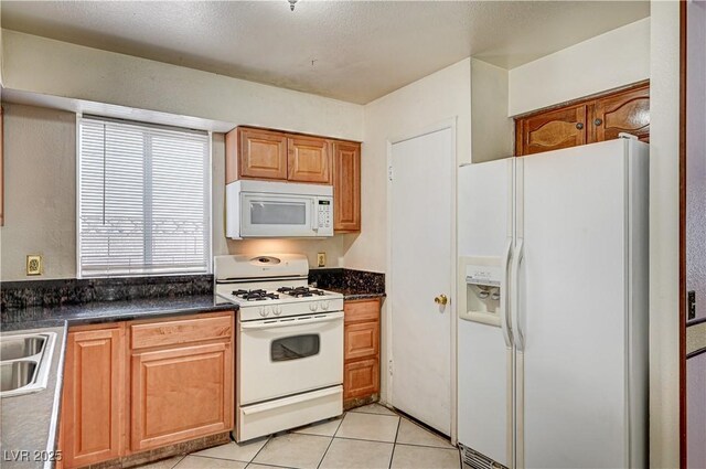 5121 Gains Mill St, Las Vegas, NV 89122 - kitchen featuring white appliances, dark countertops, light tile patterned floors, and brown cabinetry