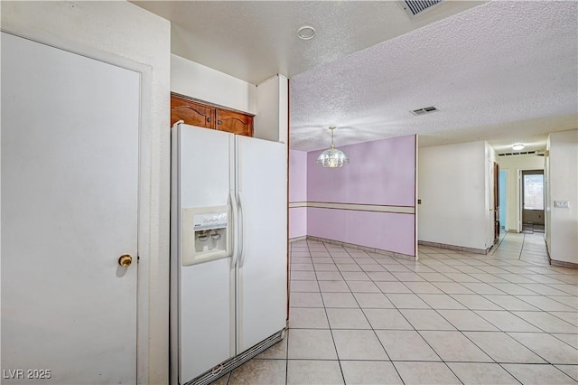 5121 Gains Mill St, Las Vegas, NV 89122 - kitchen with white fridge with ice dispenser, a textured ceiling, brown cabinetry, and light tile patterned floors