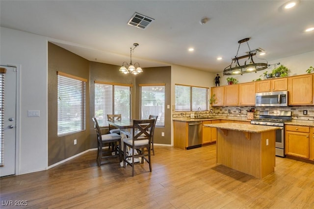 6109 Sandstone Mesa Dr, Las Vegas, NV 89130 - kitchen with stainless steel appliances, decorative backsplash, a kitchen island, light stone counters, and light wood-style flooring